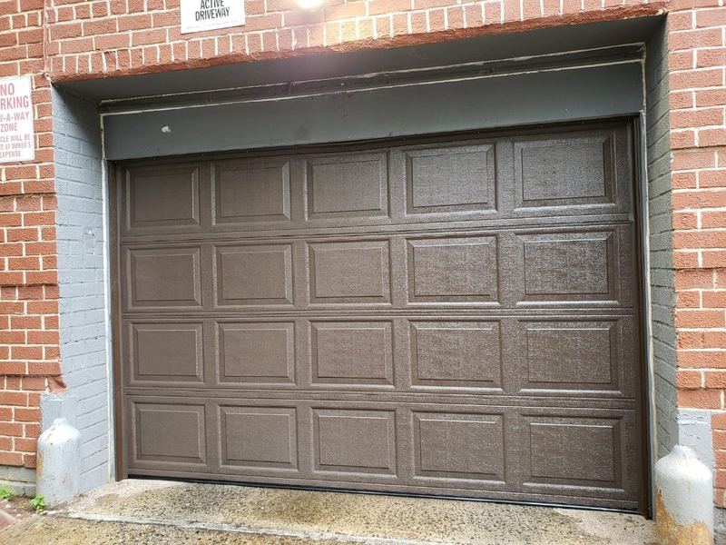 Brown raised-panel sectional garage door set in a red brick wall
